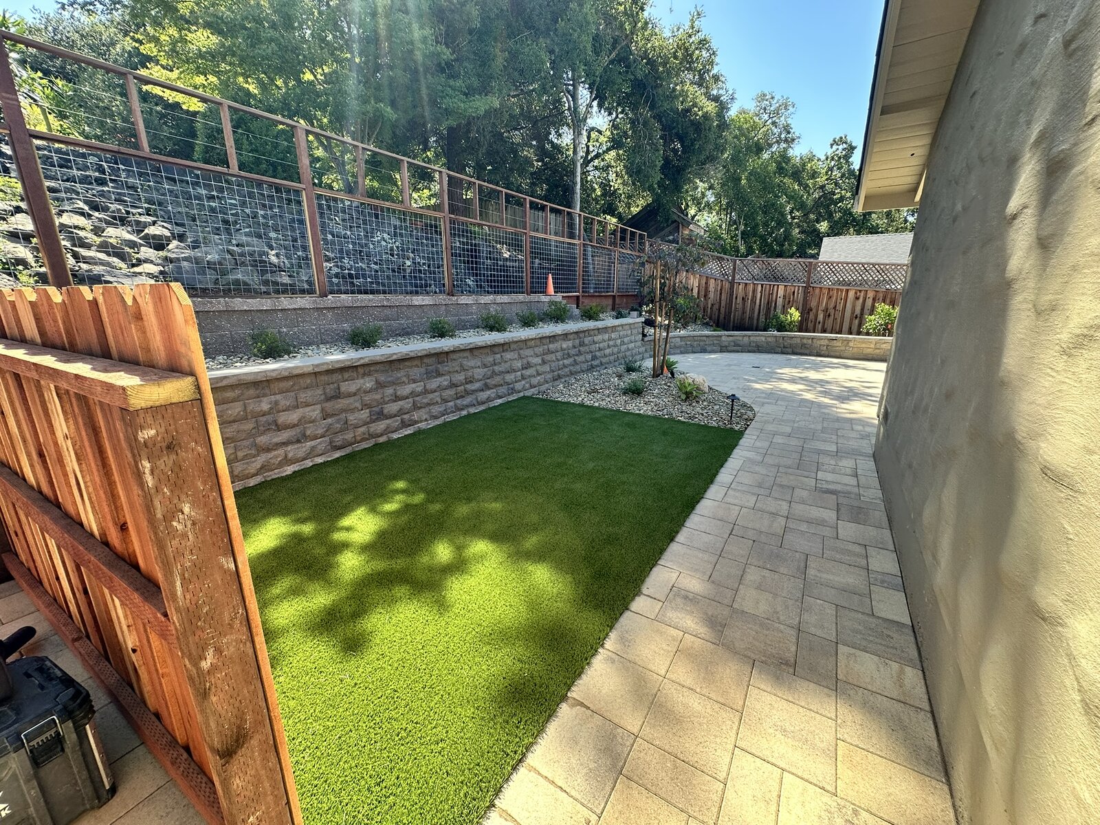 Side yard completed — synthetic turf, paver walkway, retaining wall, and wire fencing