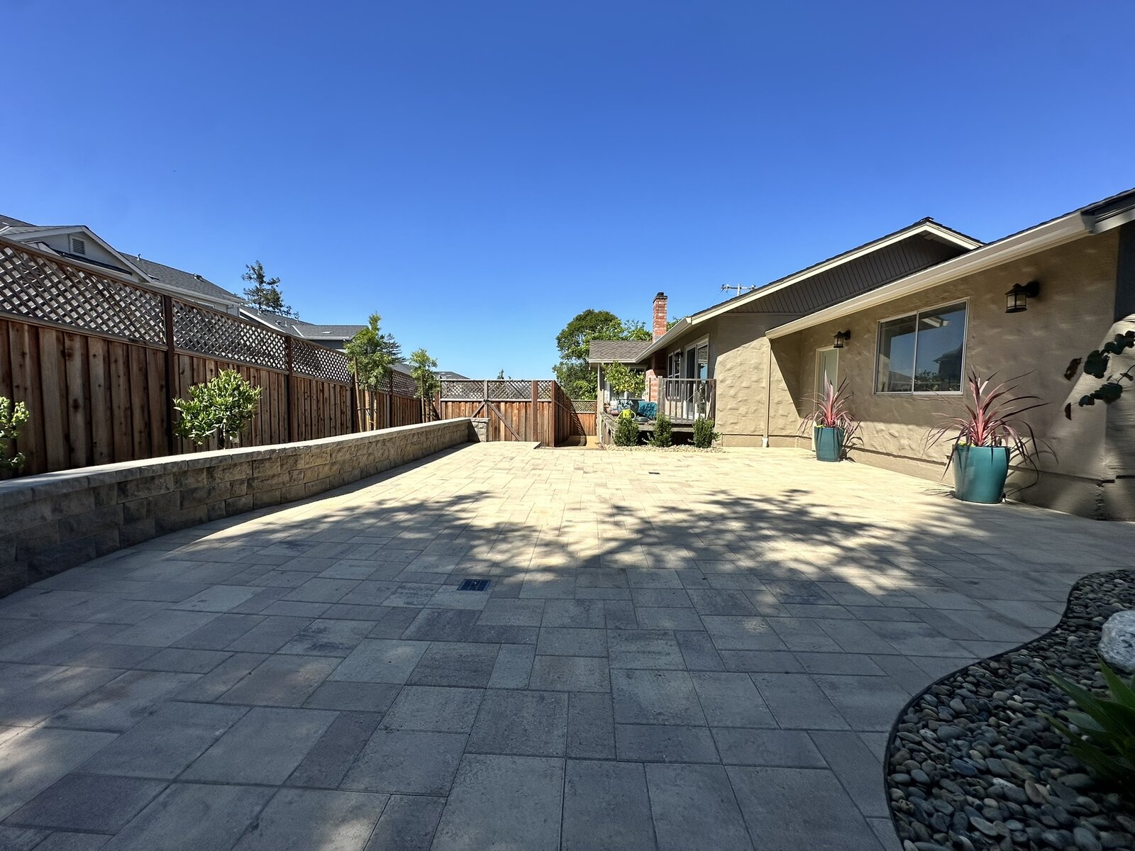 Main patio completed — paver patio with retaining wall, potted plants, and clean sightlines