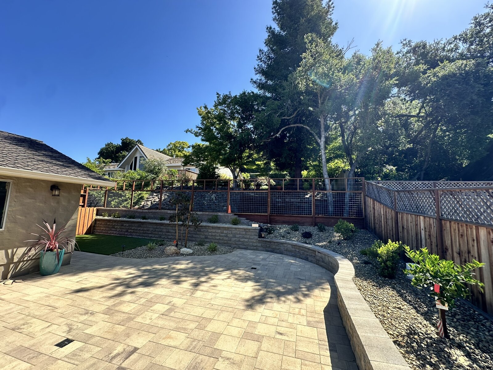 Upper patio completed — paver patio with curved seating wall, plantings, and wire fencing