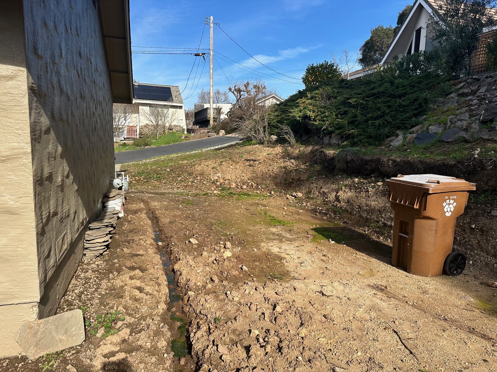 Front slope before — bare dirt with exposed utilities and no landscaping