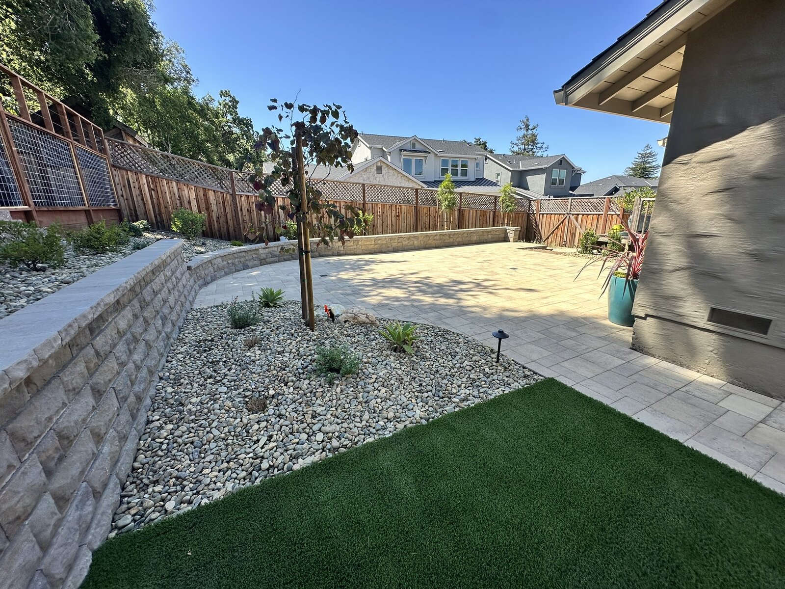 Lounge area completed — retaining wall with river rock, turf, and paver patio