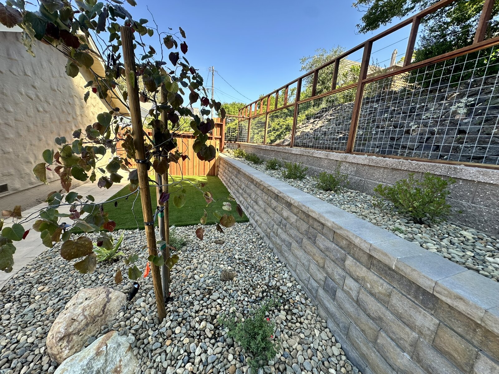 Retaining wall completed — block wall with young vine, synthetic turf, and gravel drainage