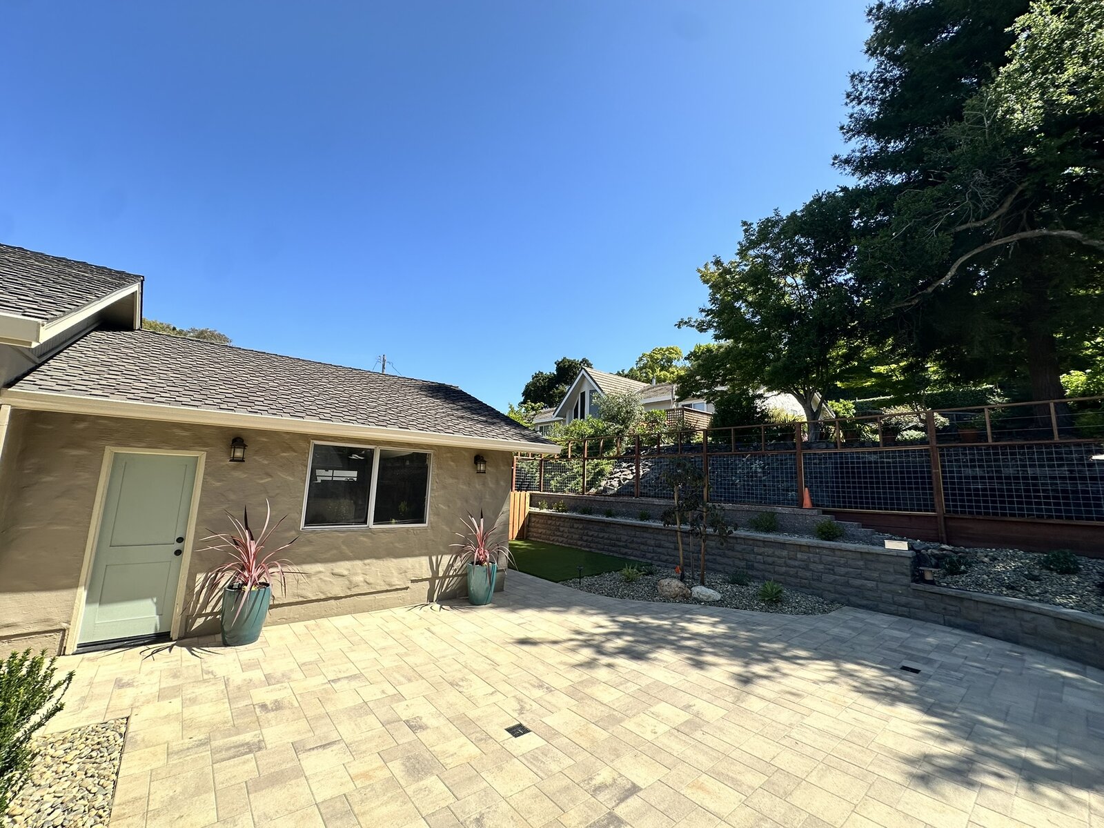 Deck and stairs completed — composite deck, cable railing, paver patio, and hillside plantings